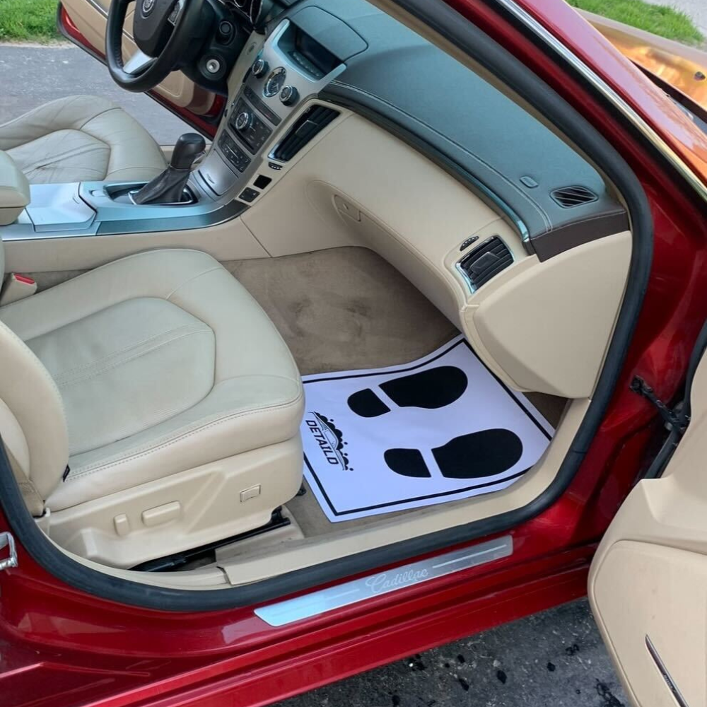 An auto detailing technician washing the front exterior of a white mercedes-benz car. The white foam soap bubbles up in the front grill of the car.