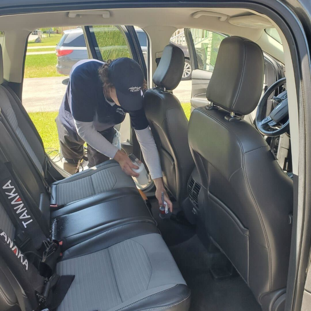 A car detailer vacuuming the interior of an SUV.