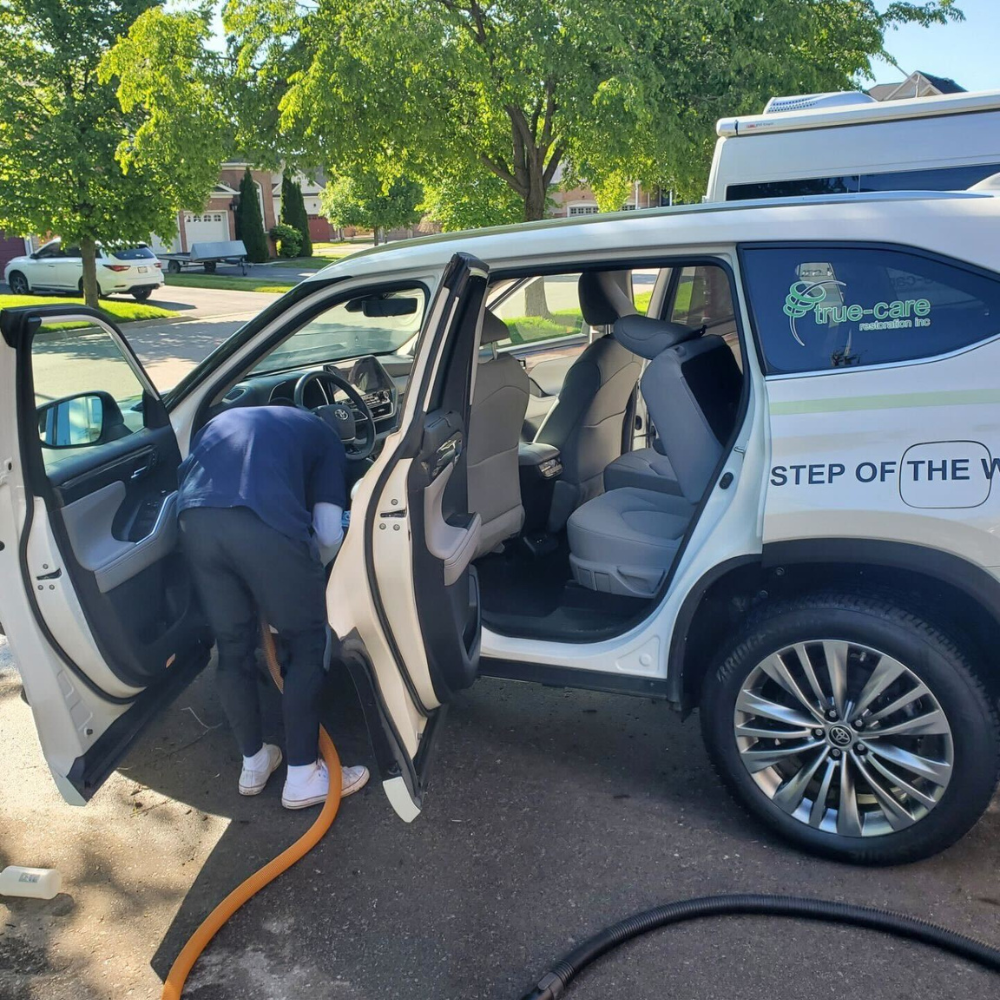 A car detailer vacuuming the front interior of an SUV in a driveway.