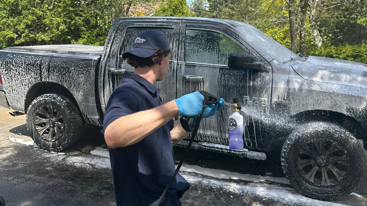 A car detailer washing a truck using a pressure washer