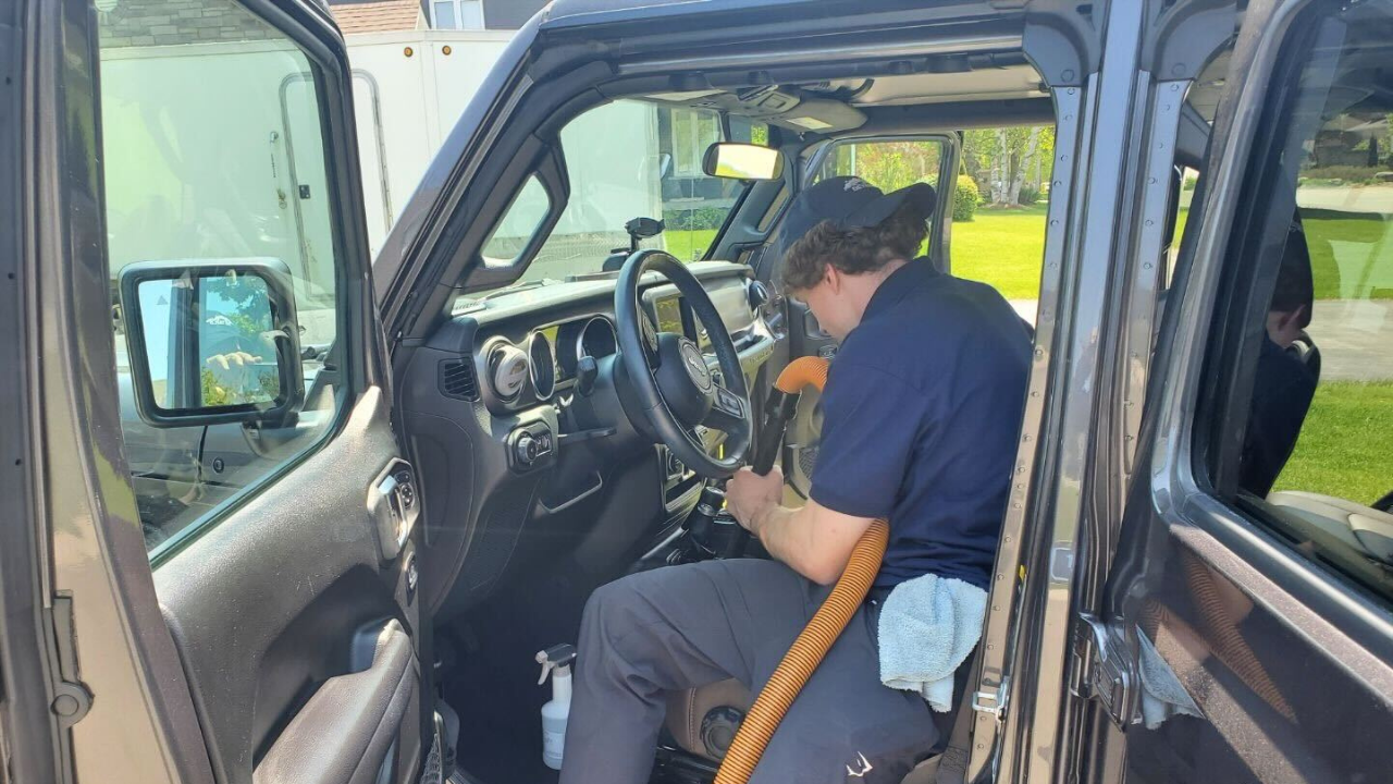 A car detailer using a vacuum to clean the interior of a vehicle.